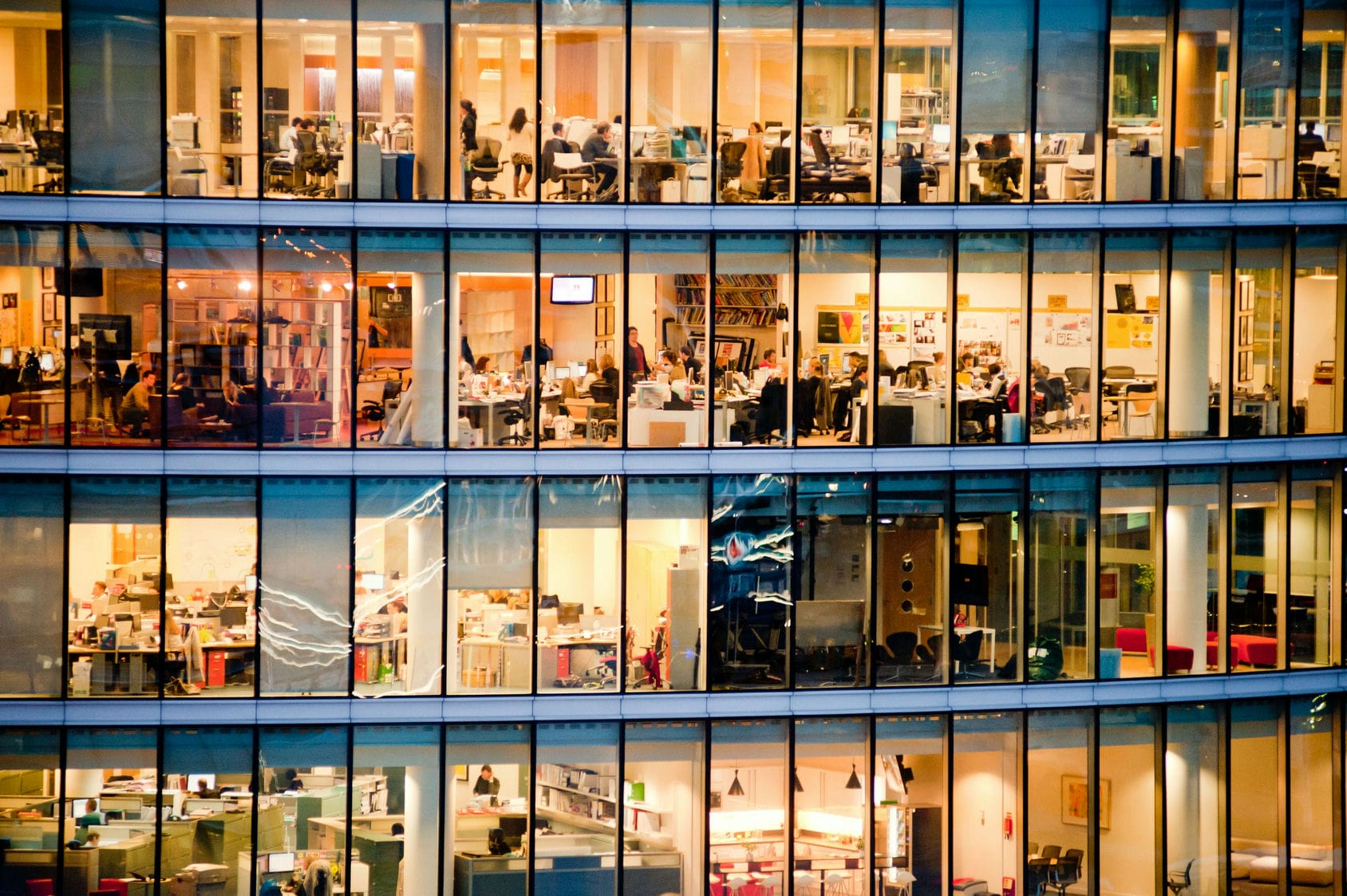 An office building lit up at dusk, with people working within